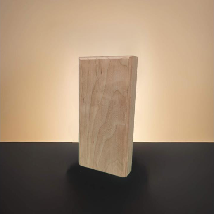 A rectangular block of natural light cherry wood with visible grain, standing upright on a dark surface against a warm beige gradient background.