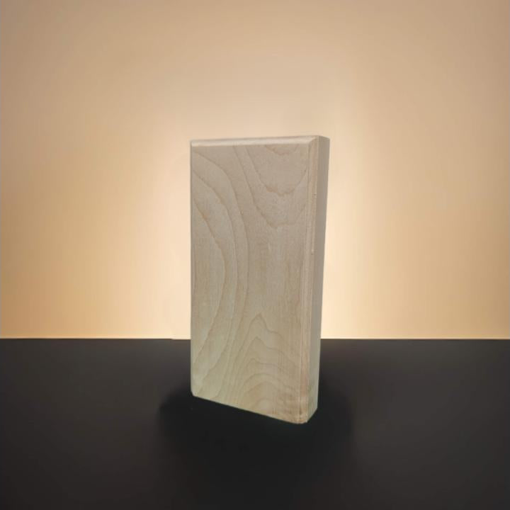 A rectangular block of light-colored maple wood with visible grain, standing upright on a dark surface against a warm beige background.