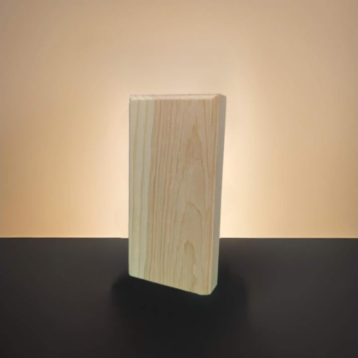 A rectangular block of unfinished pine wood with visible grain, standing upright on a dark surface against a warm beige gradient background.