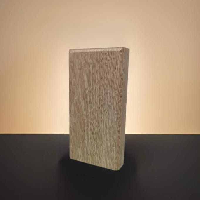 A rectangular block of light red oak wood with visible grain, standing upright on a black surface against a warm beige gradient background.