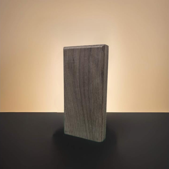 A rectangular dark walnut wood block with a visible wood grain texture, standing upright on a dark surface against a warm beige gradient background.
